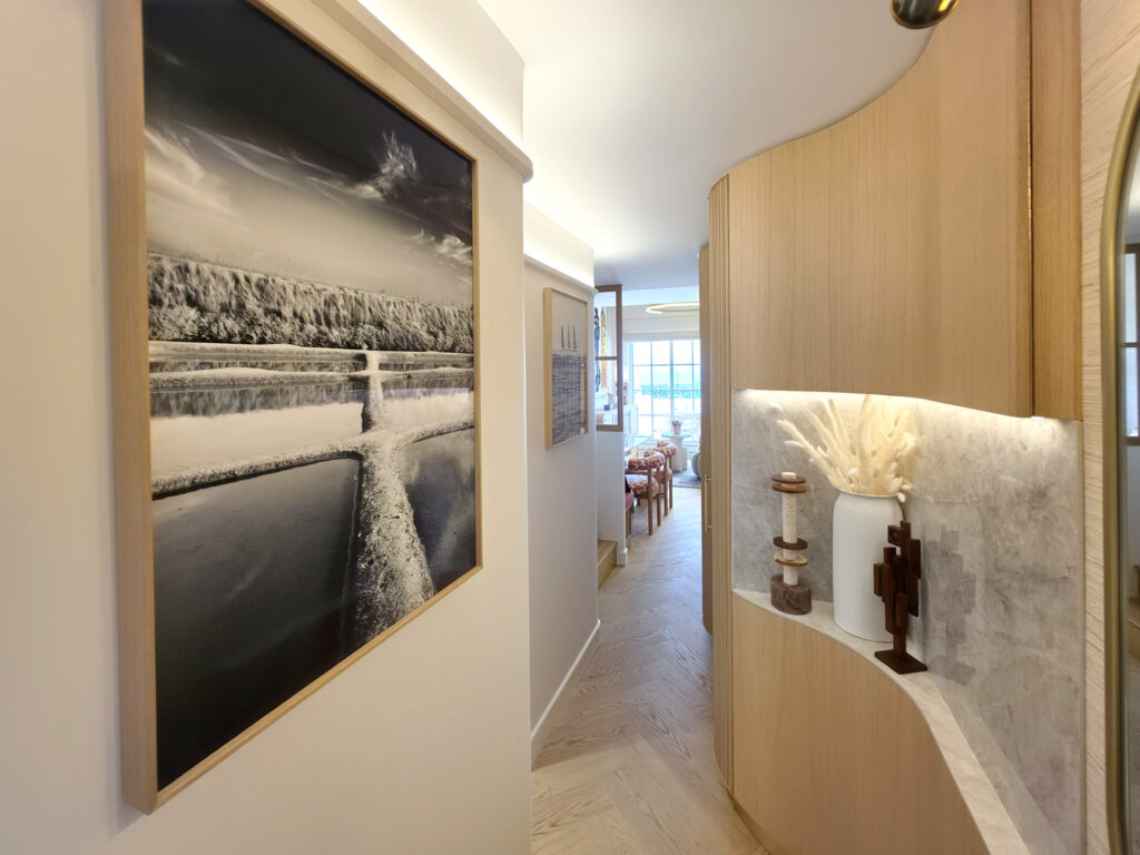 Couloir d'entrée en courbe avec meuble sur mesure rétroéclairé, niche en marbre clair et photographie noir et blanc de Yann Lecomte.