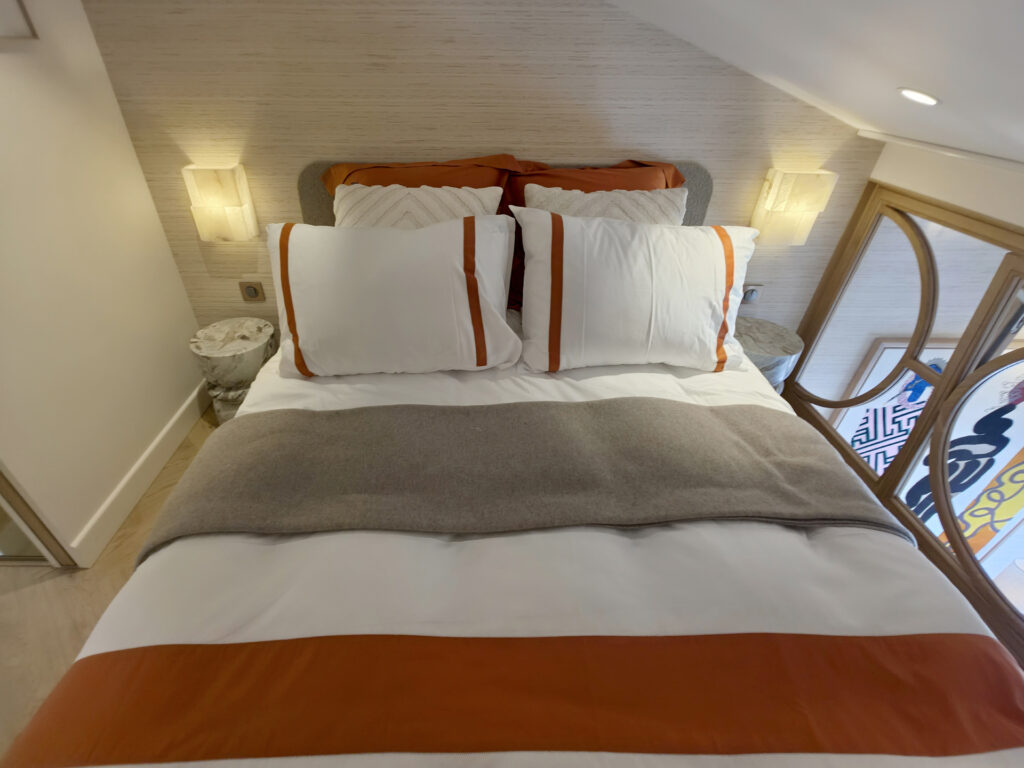 Chambre en mezzanine sous rampant avec lit coffre terracotta, appliques en albâtre, tables en marbre et verrière sur mesure en bois ouvrant sur le salon.