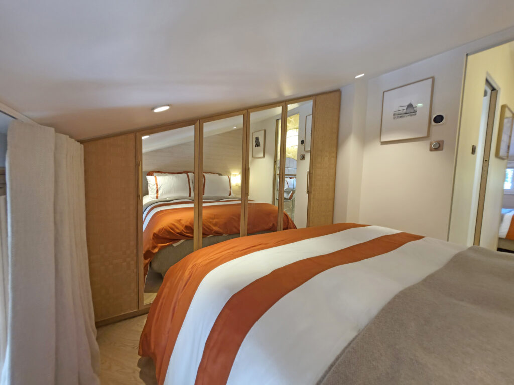 Chambre mezzanine sous pente avec grand placard sur mesure à portes miroir grossissantes et linge de lit terracotta et blanc.