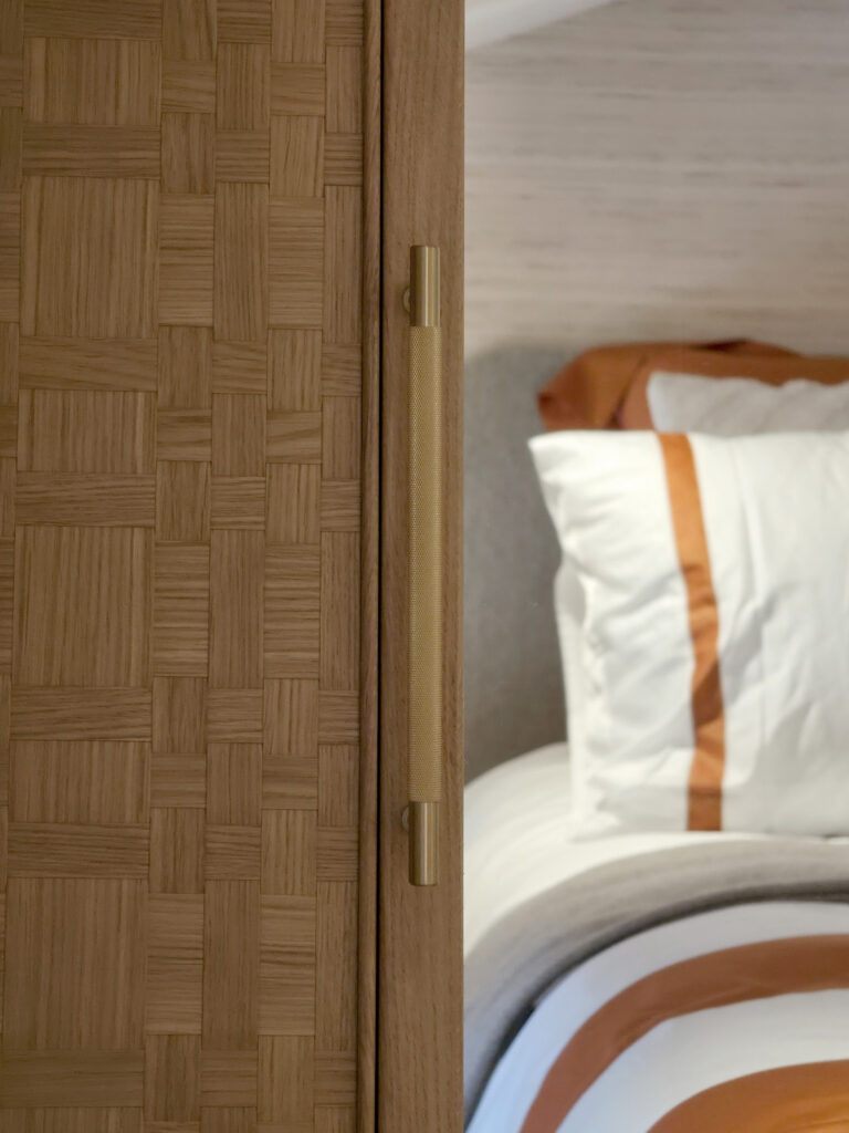 Détail d'une poignée de placard moletée en laiton doré brossé fixée sur un panneau de dressing en bois tressé.