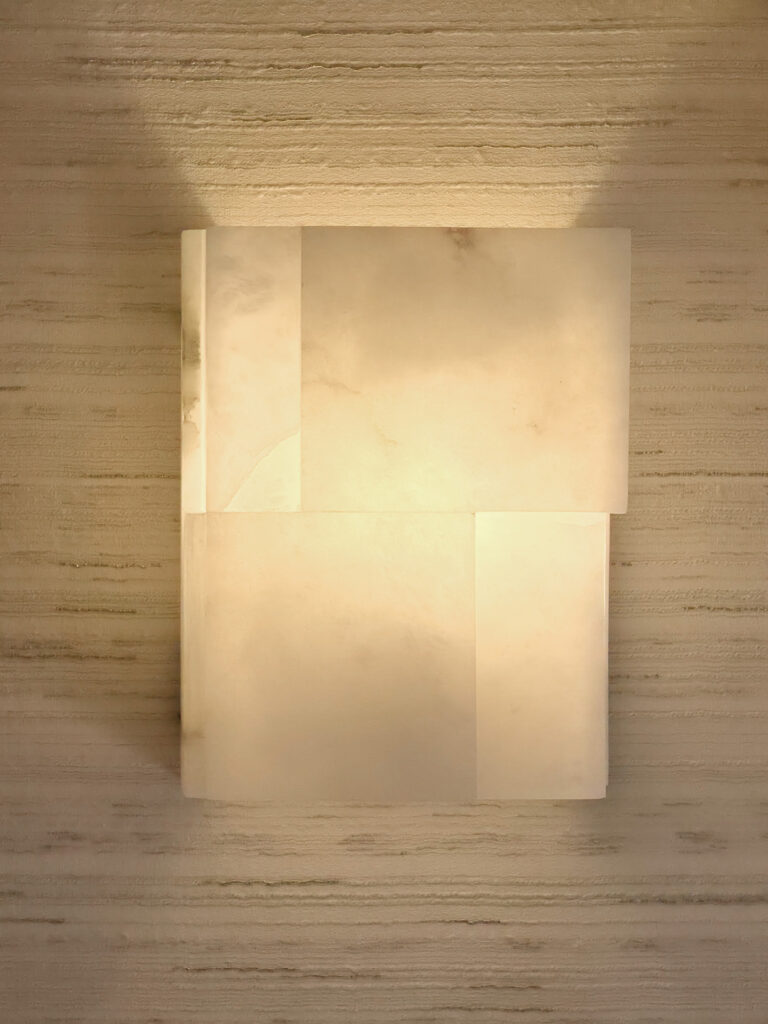 Applique murale rectangulaire en pierre d'albâtre translucide rétroéclairée sur papier peint effet fil-à-fil beige.