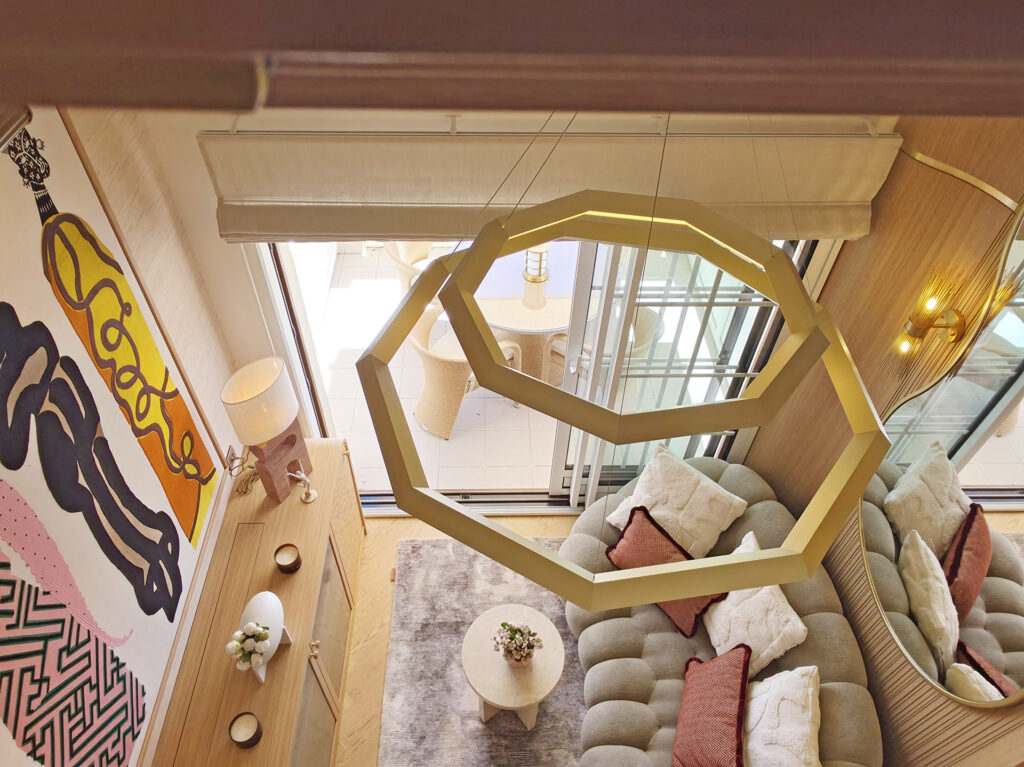 Vue spectaculaire en contre-plongée depuis la mezzanine montrant la suspension hexagonale dorée, le canapé Curve et la terrasse extérieure.