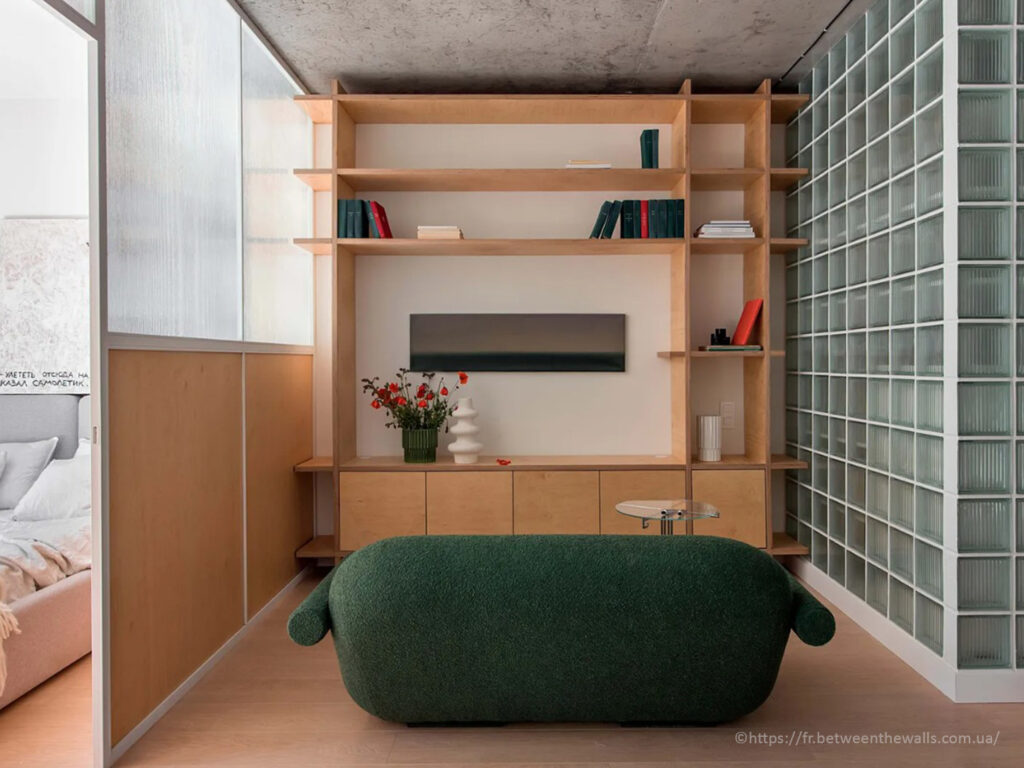 Salon contemporain avec canapé vert forêt, bibliothèque ouverte en contreplaqué et cloison vitrée par Between the Walls.
