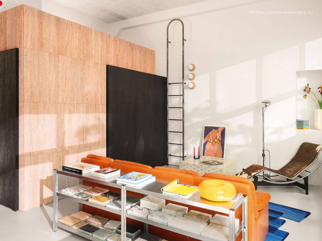 Espace séjour d'architecte avec grand bloc mural revêtu de travertin rosé, canapé cuir orange et échelle noire par Atelierzero.