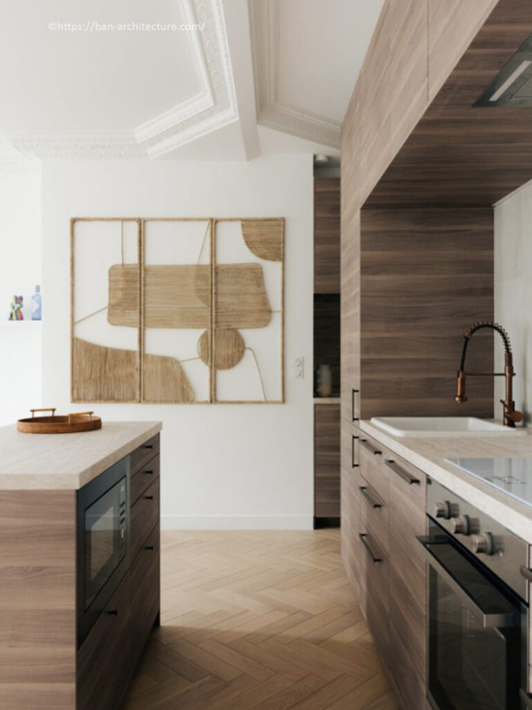 Cuisine linéaire en bois de noyer avec îlot central, robinetterie cuivrée et tableau mural tressé par Bän Architecture.