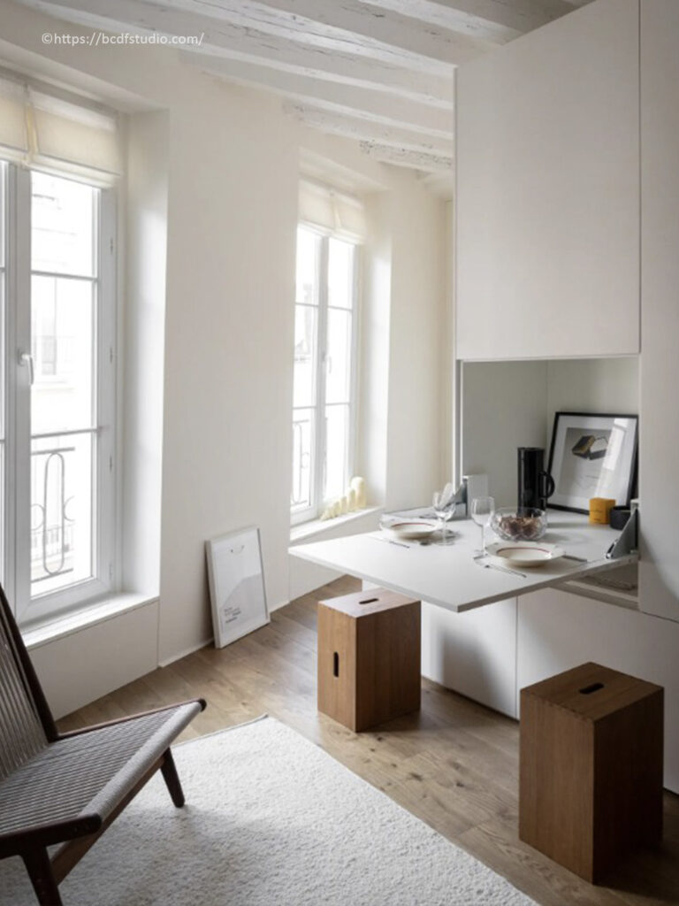 Studio épuré avec table repas escamotable intégrée dans un grand meuble blanc sur mesure par BCDF Studio.